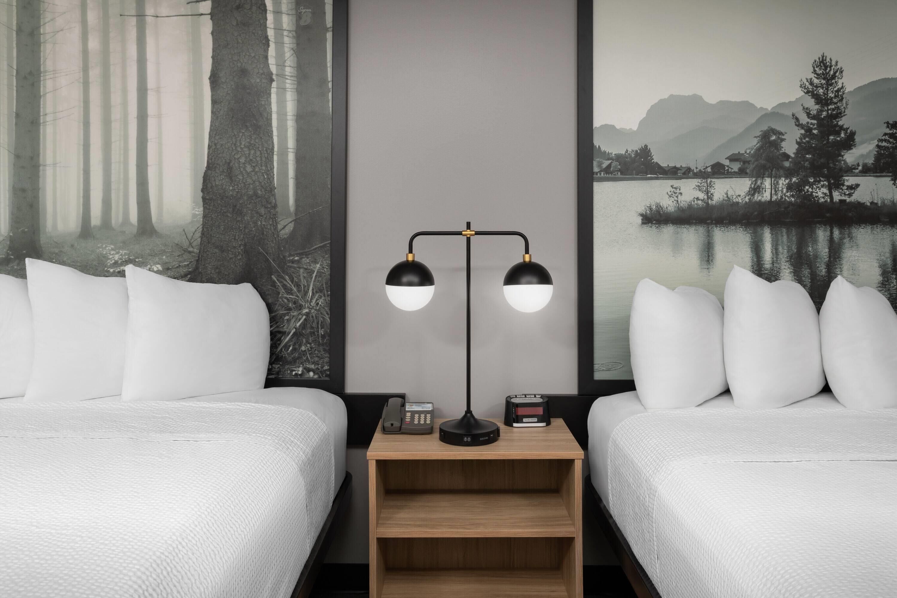 Une chambre d’hôtel avec deux lits, une table de chevet avec une lampe, un téléphone et une horloge numérique.
