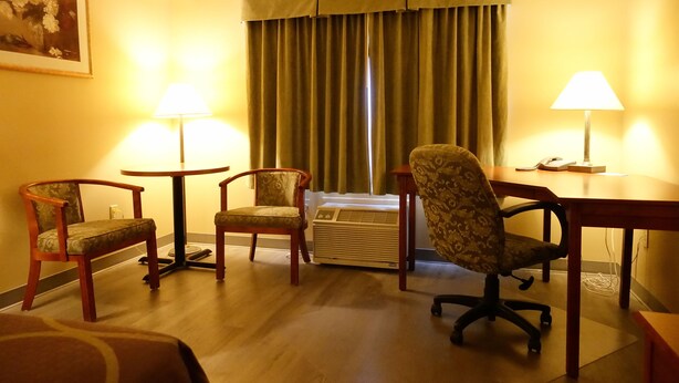 A hotel room with a wooden floor, two armchairs, a desk, a lamp, and a large window with curtains.