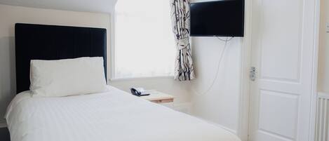 Ein ordentlich bezogenes Bett mit schwarzem Kopfteil, ein Nachttisch mit Telefon und ein an der Wand befestigter Fernseher.