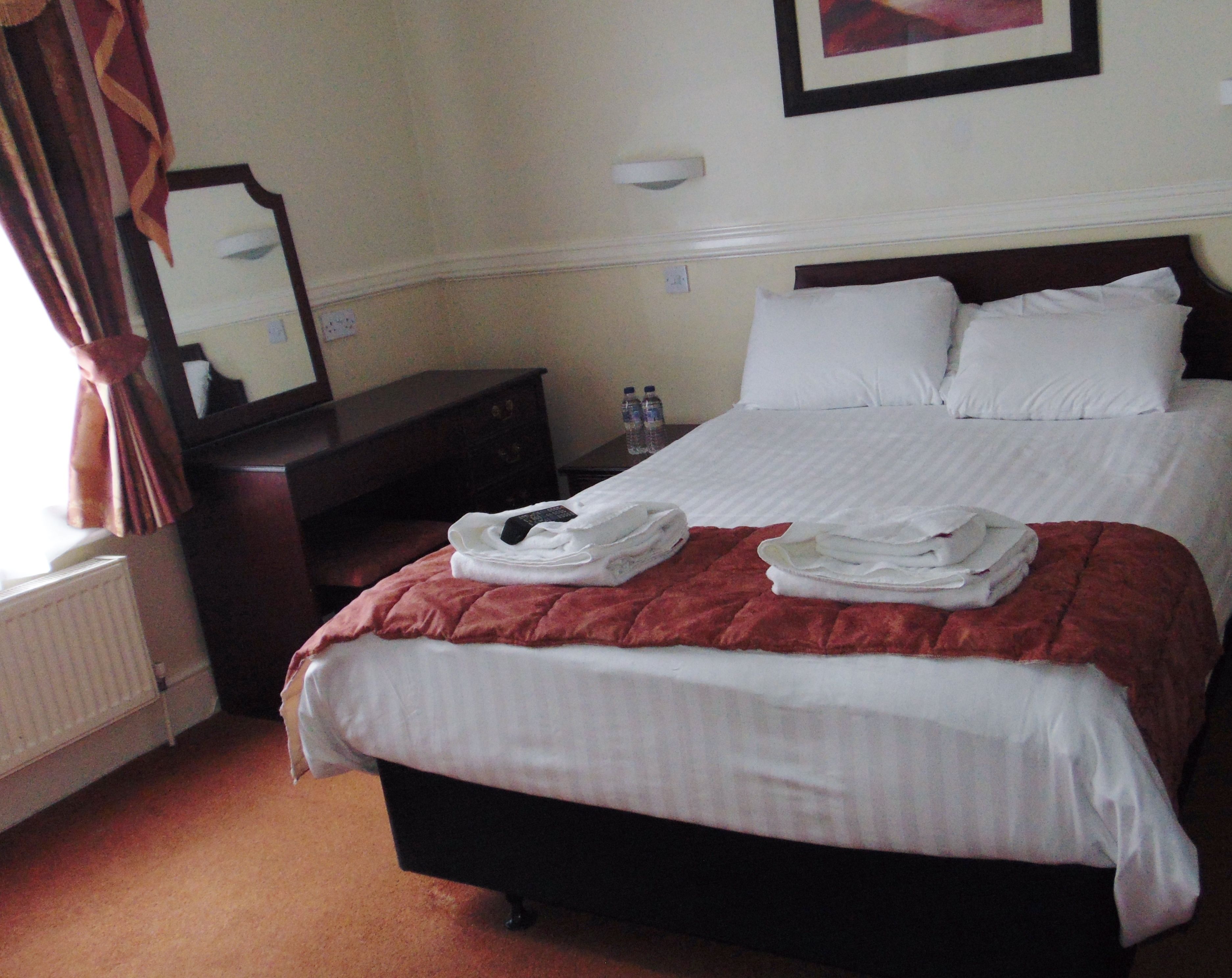 A hotel room with a neatly made bed, a dresser, a mirror, and a framed picture on the wall.