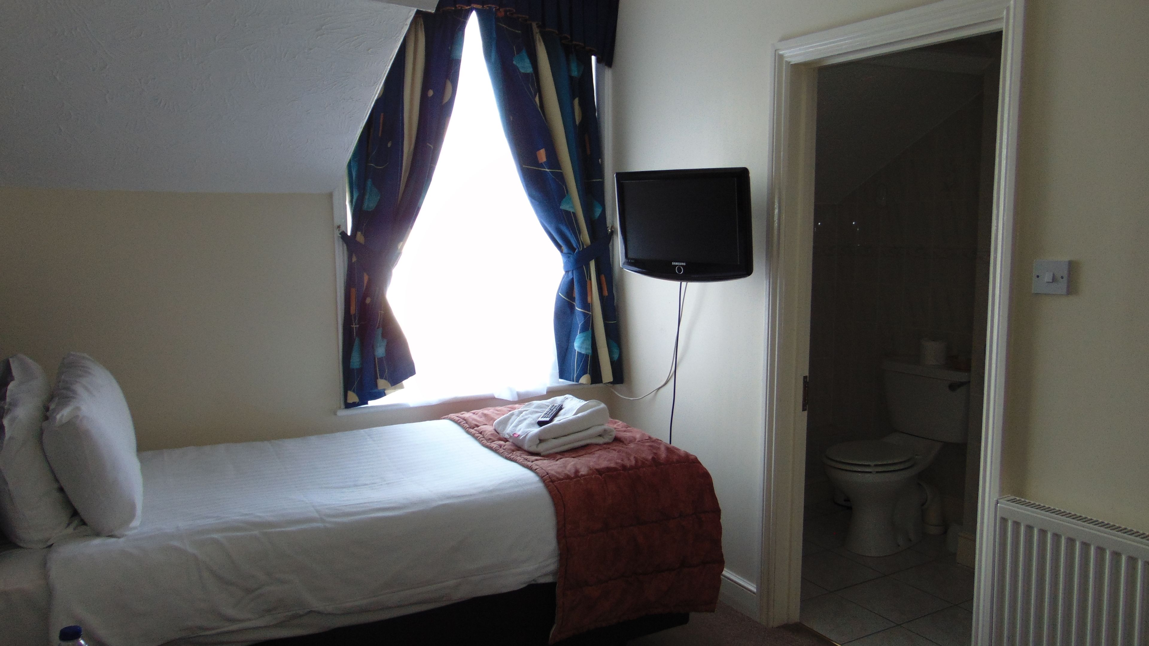 A hotel room with a bed, a TV mounted on the wall, a window with curtains, and a view of the bathroom.