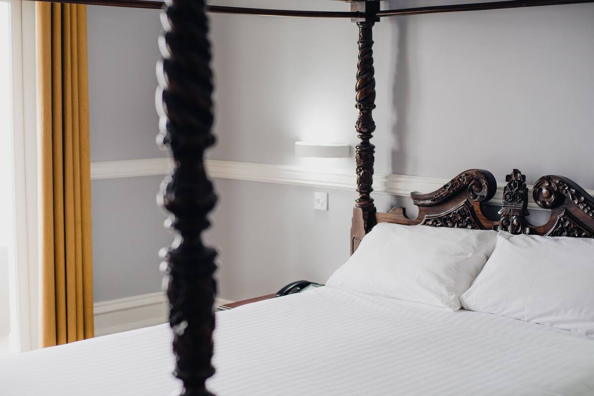 A four-poster bed with white linens and a wooden headboard.