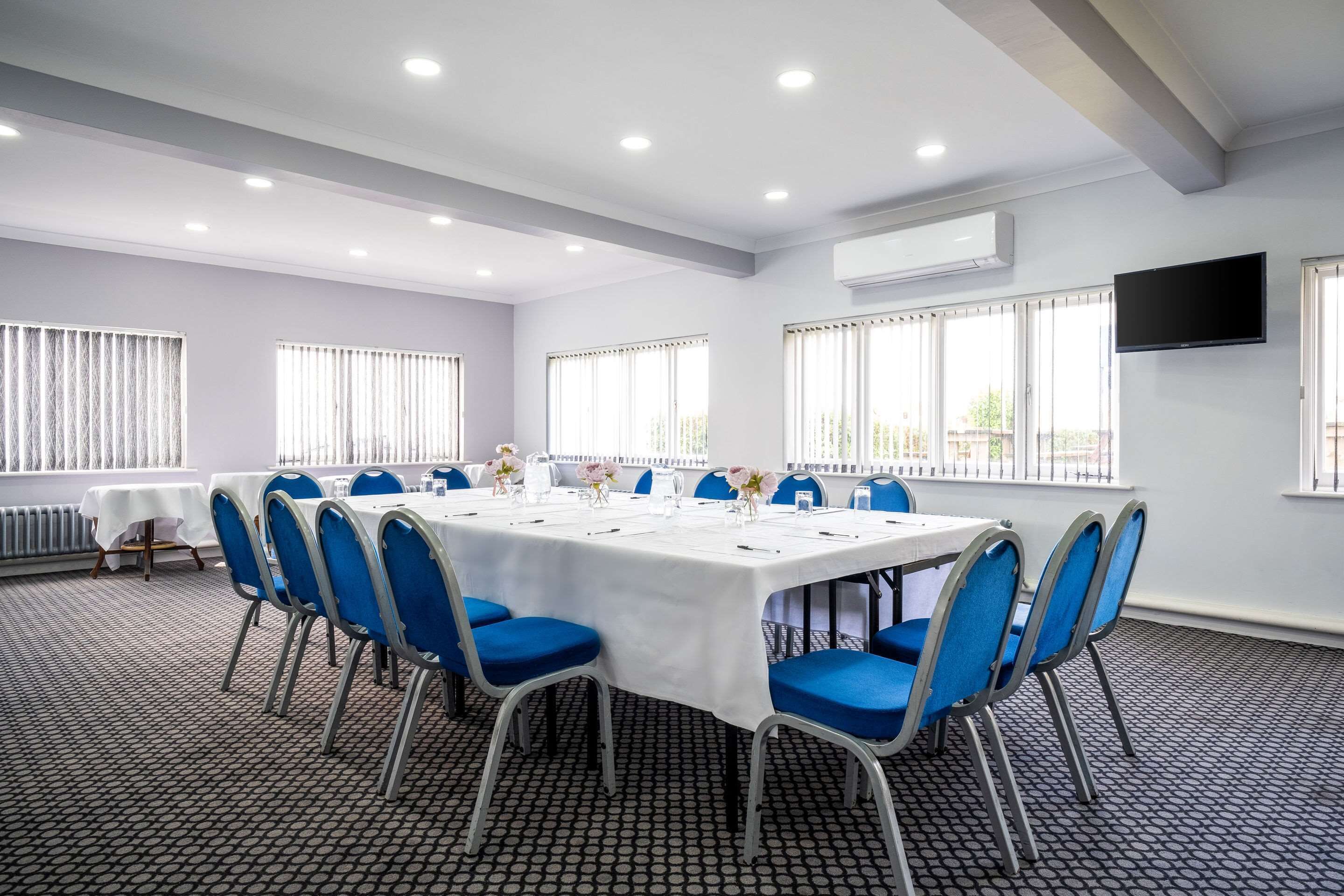 A conference room with a long table, blue chairs, and large windows with blinds.