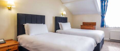 Een hotelkamer met twee bedden, een houten nachtkastje, een lamp en een raam met blauwe gordijnen.