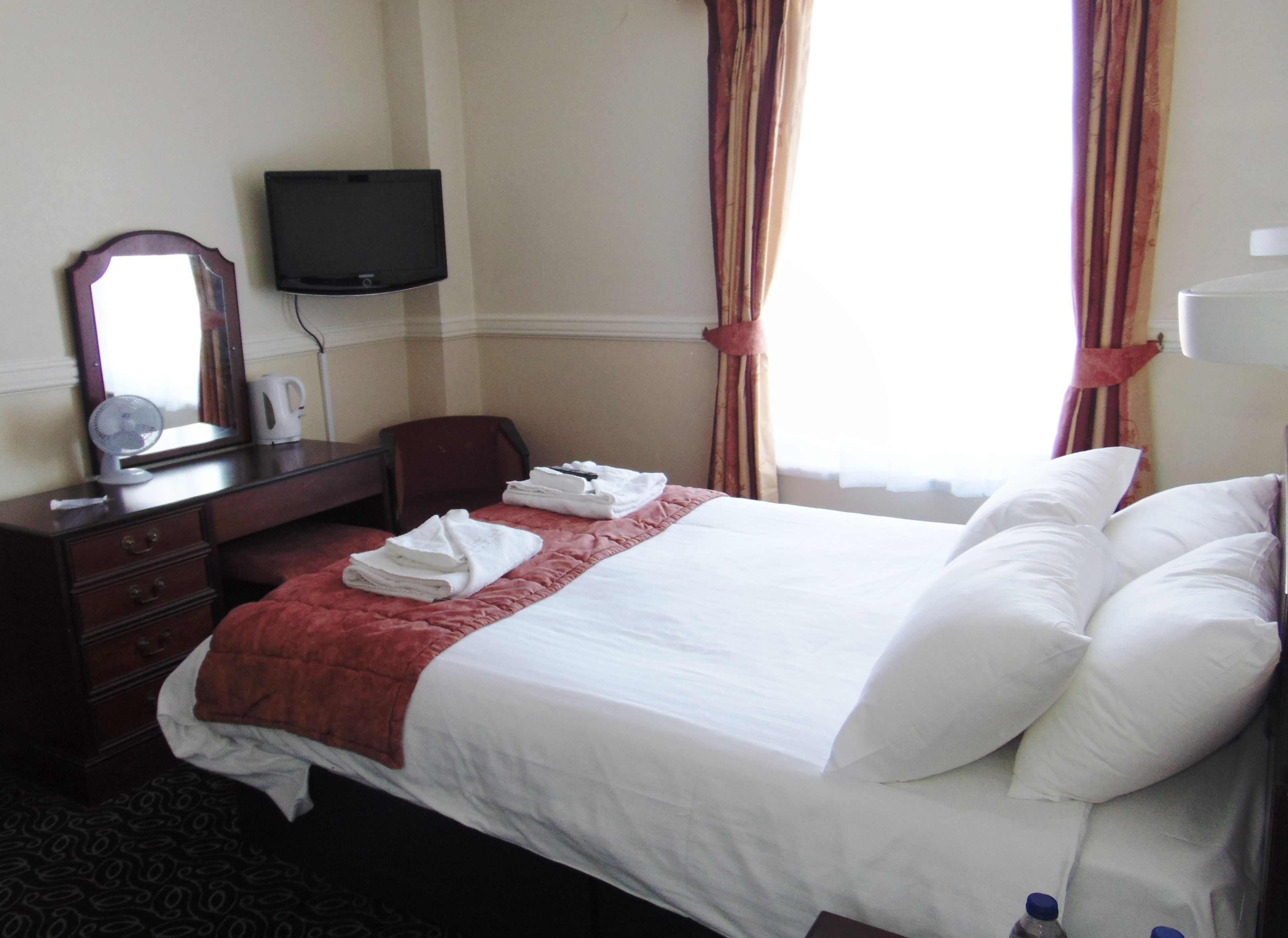 A hotel room with a bed, a desk, a chair, a television, and a window with curtains.