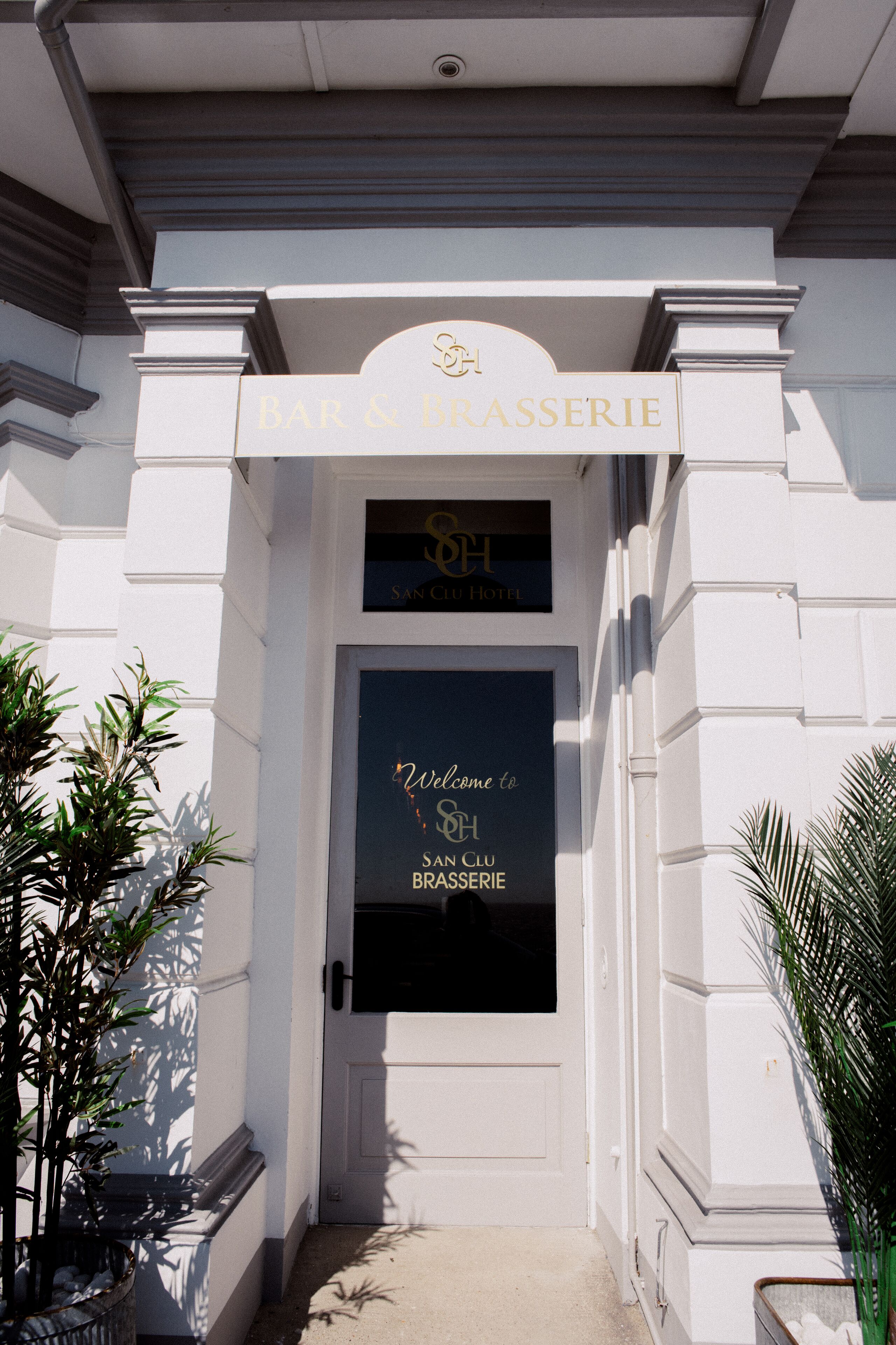 L’entrée d’un bar et d’une brasserie, avec une enseigne au-dessus de la porte et un message d’accueil à l’intérieur.