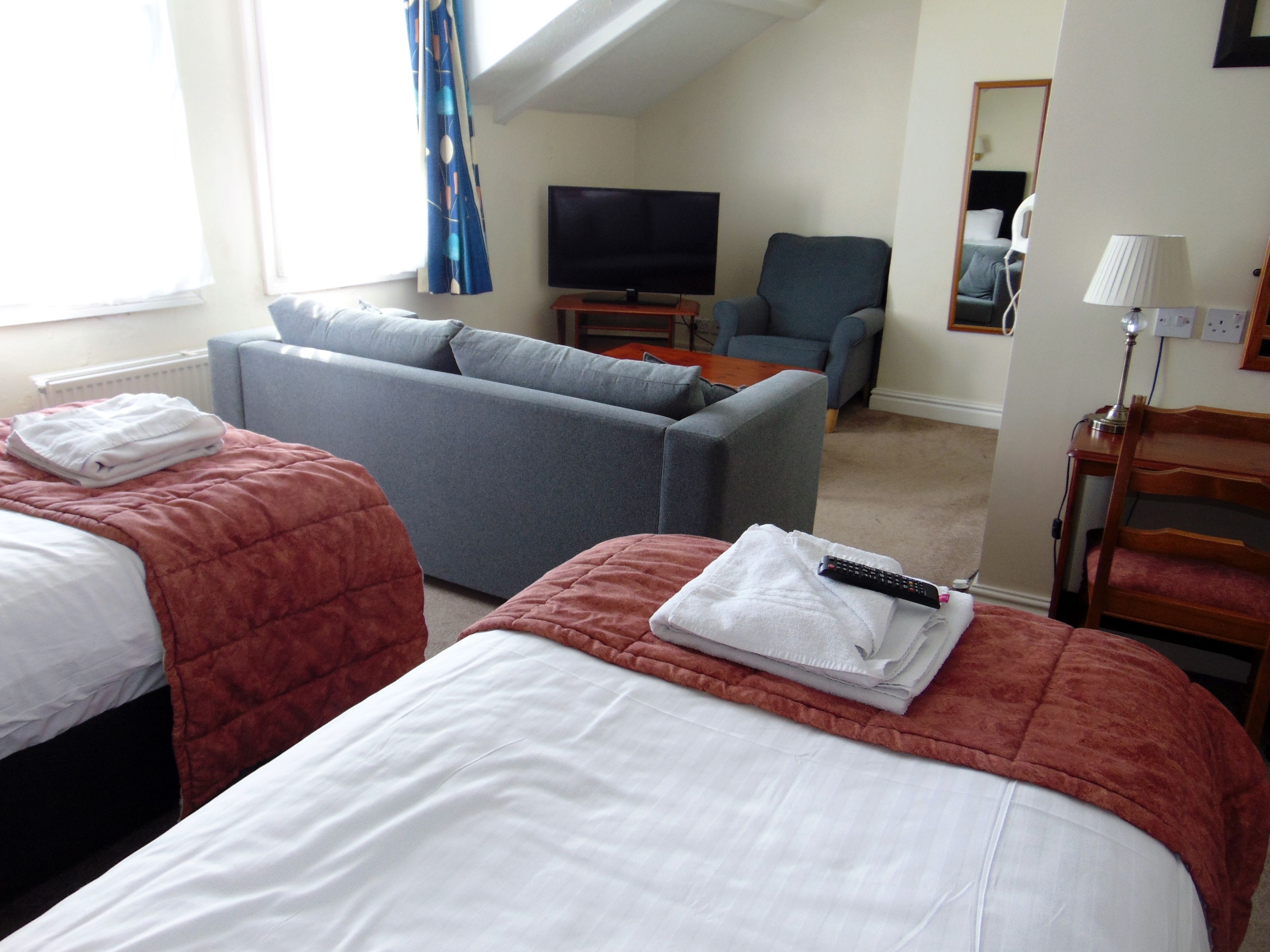 A hotel room with two beds, a sofa, a TV, and a mirror.