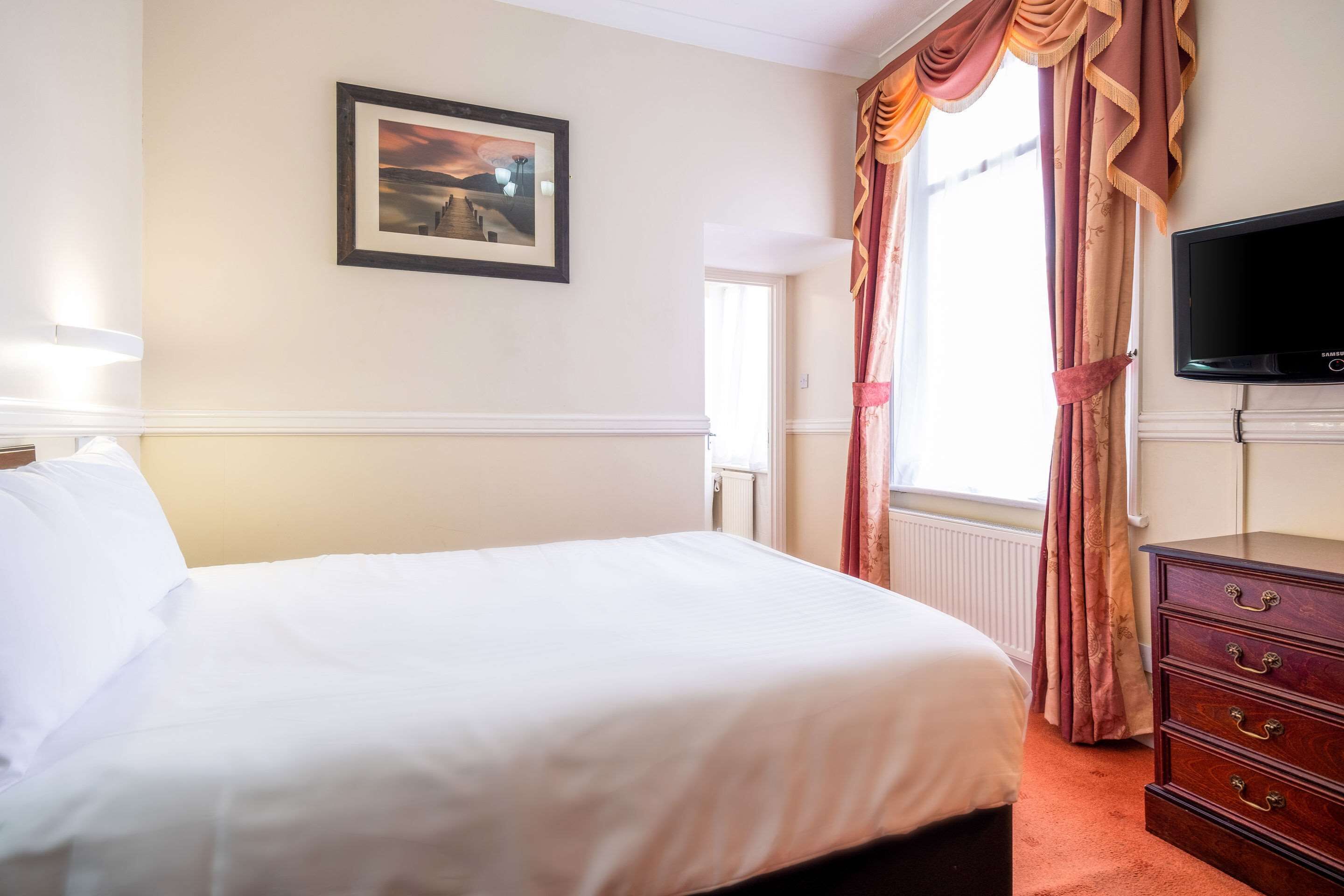 Una habitación de hotel con una cama, un aparador, un televisor y un cuadro en la pared.