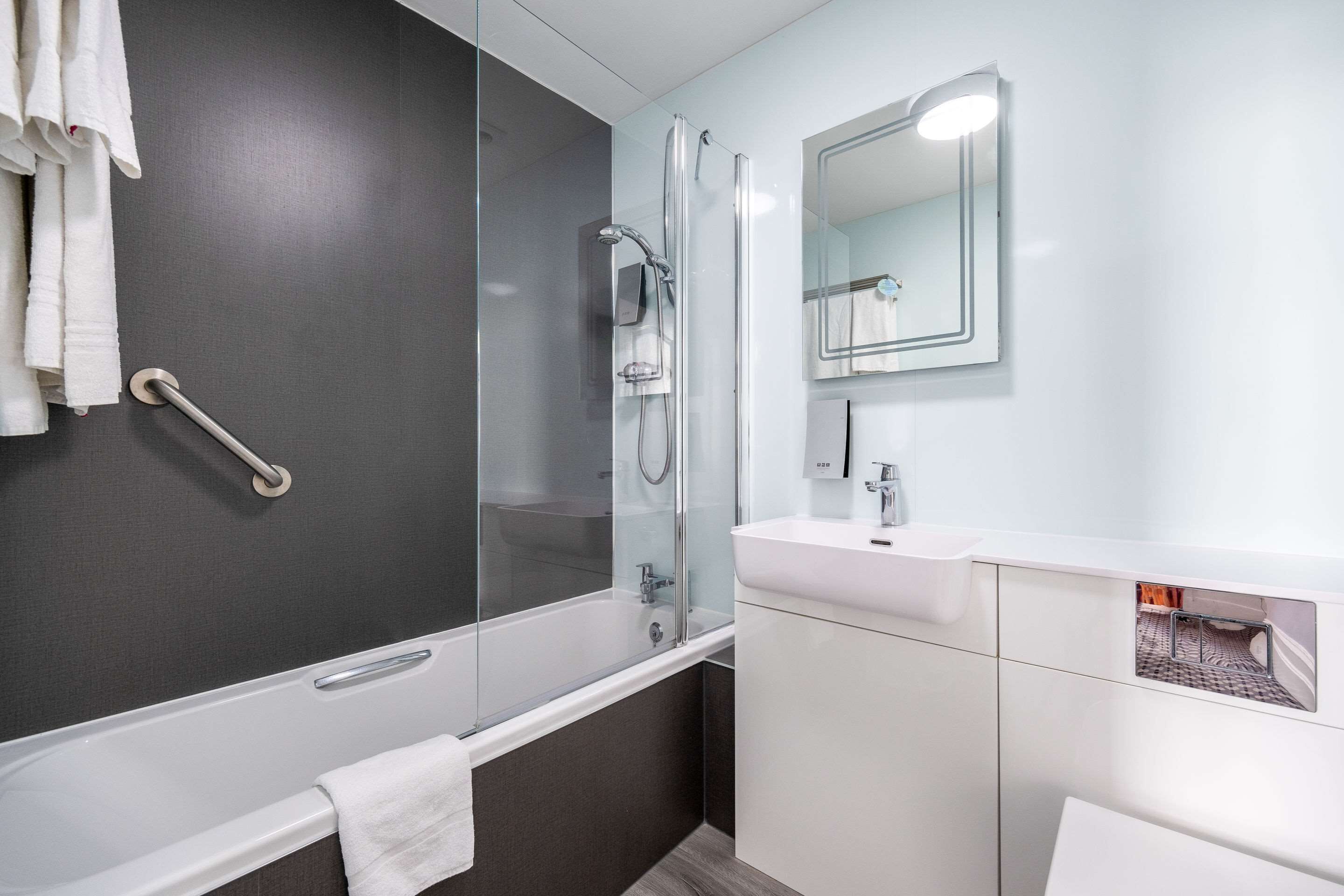 A modern bathroom with a glass-enclosed shower, a white sink, and a mirror with a light above it.