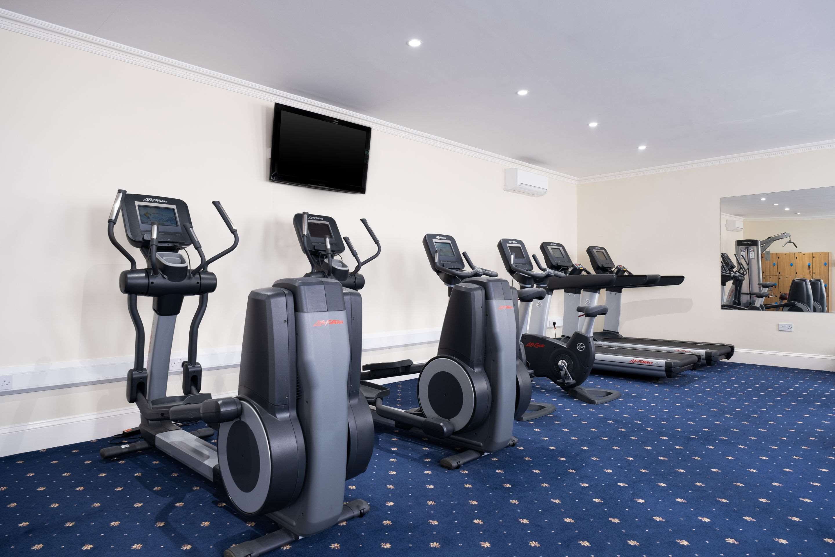 Une salle de sport équipée de tapis de course, de vélos elliptiques et d’un mur recouvert de miroirs.
