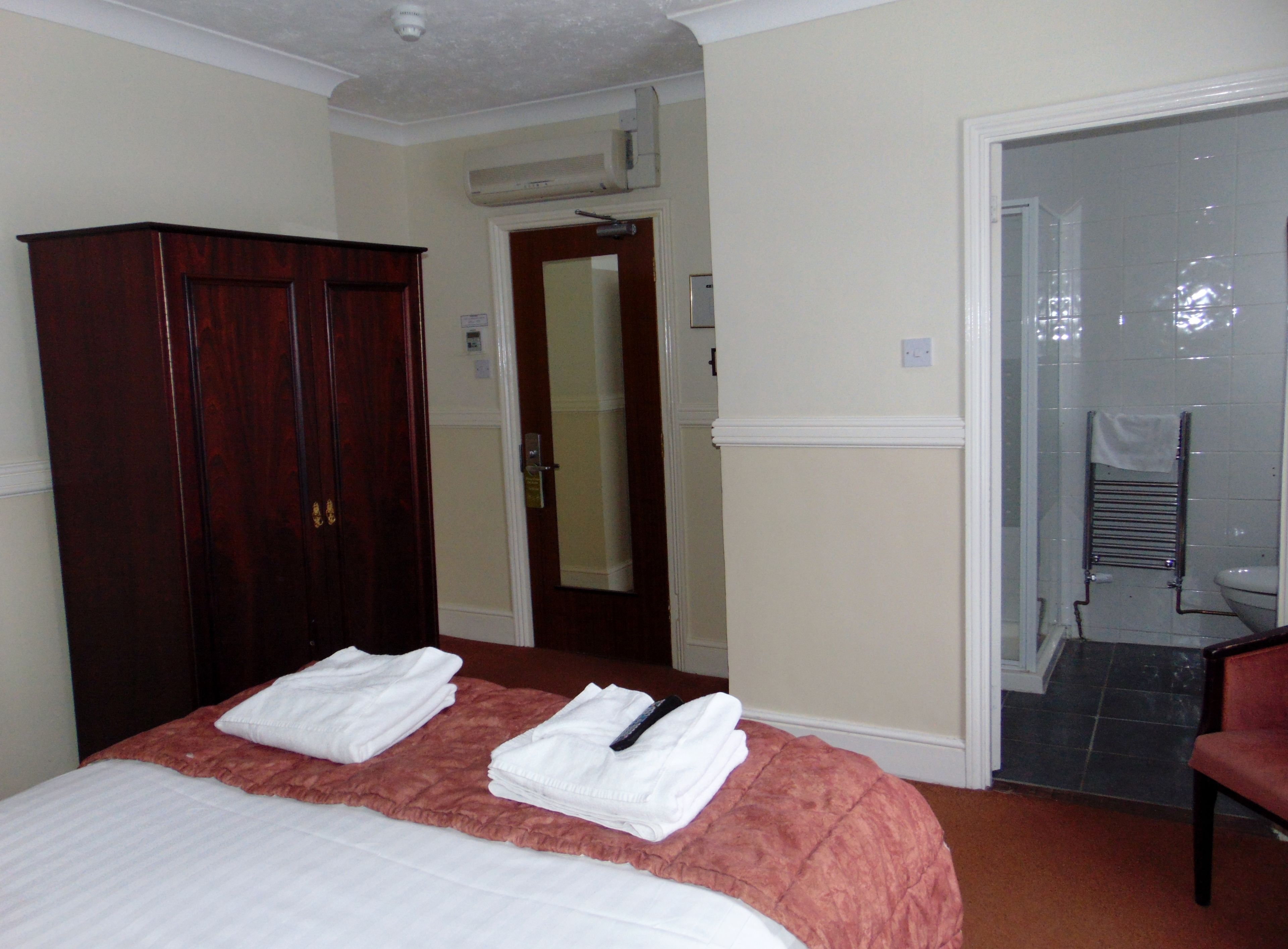 A hotel room with a bed, a wardrobe, a bathroom with a shower, and a chair.