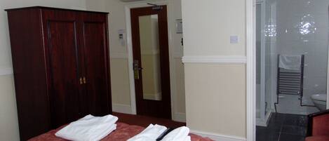 A hotel room with a bed, a wardrobe, a bathroom with a shower, and a chair.
