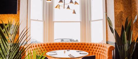 A corner seating area with a tufted orange sofa, a round table, and chairs.