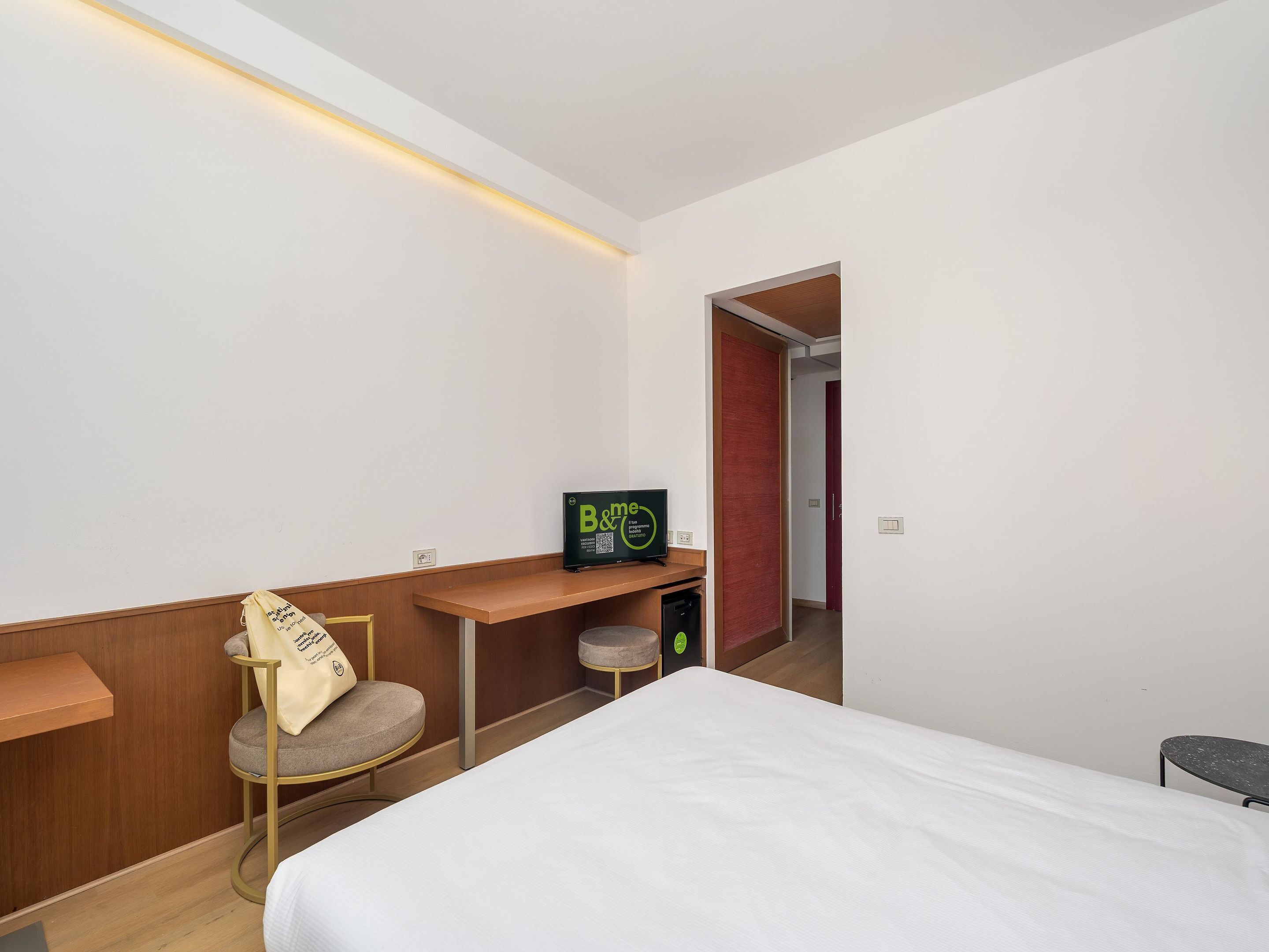 Ein Hotelzimmer mit einem Bett, einem Schreibtisch mit Computer, einem Sessel und einem kleinen Hocker.