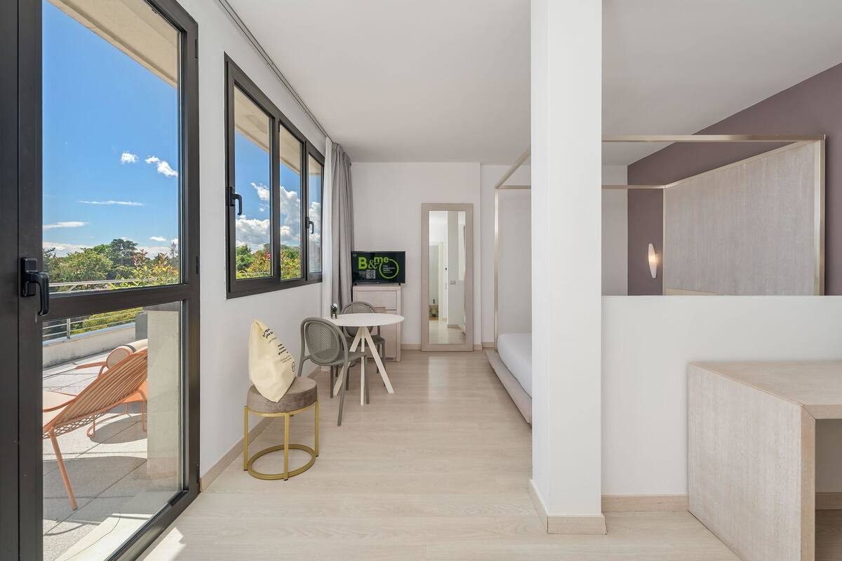 A modern apartment with large windows, a dining area, a TV, and a balcony.