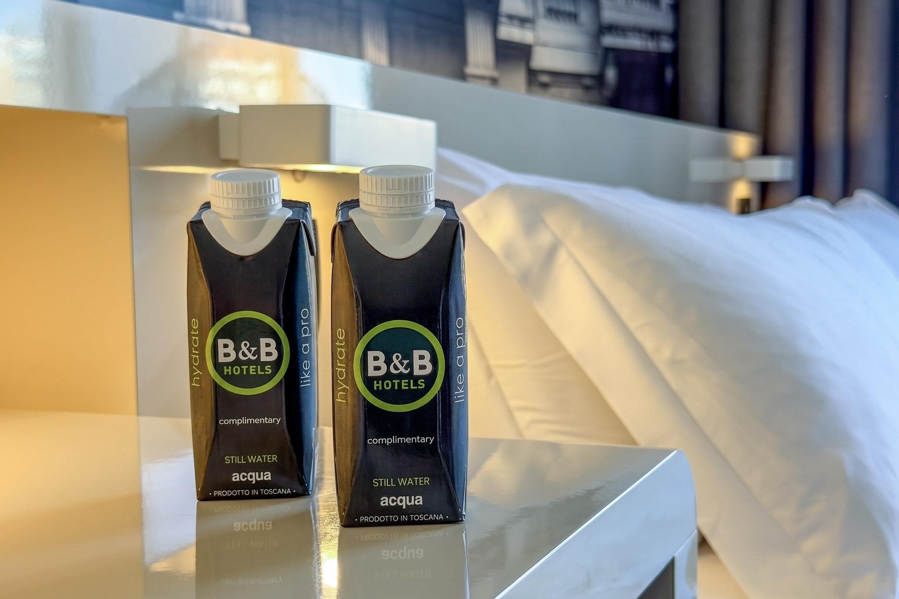 Dos cartones de agua y zumo con la marca B&B Hotels sobre una mesa de habitación de hotel.