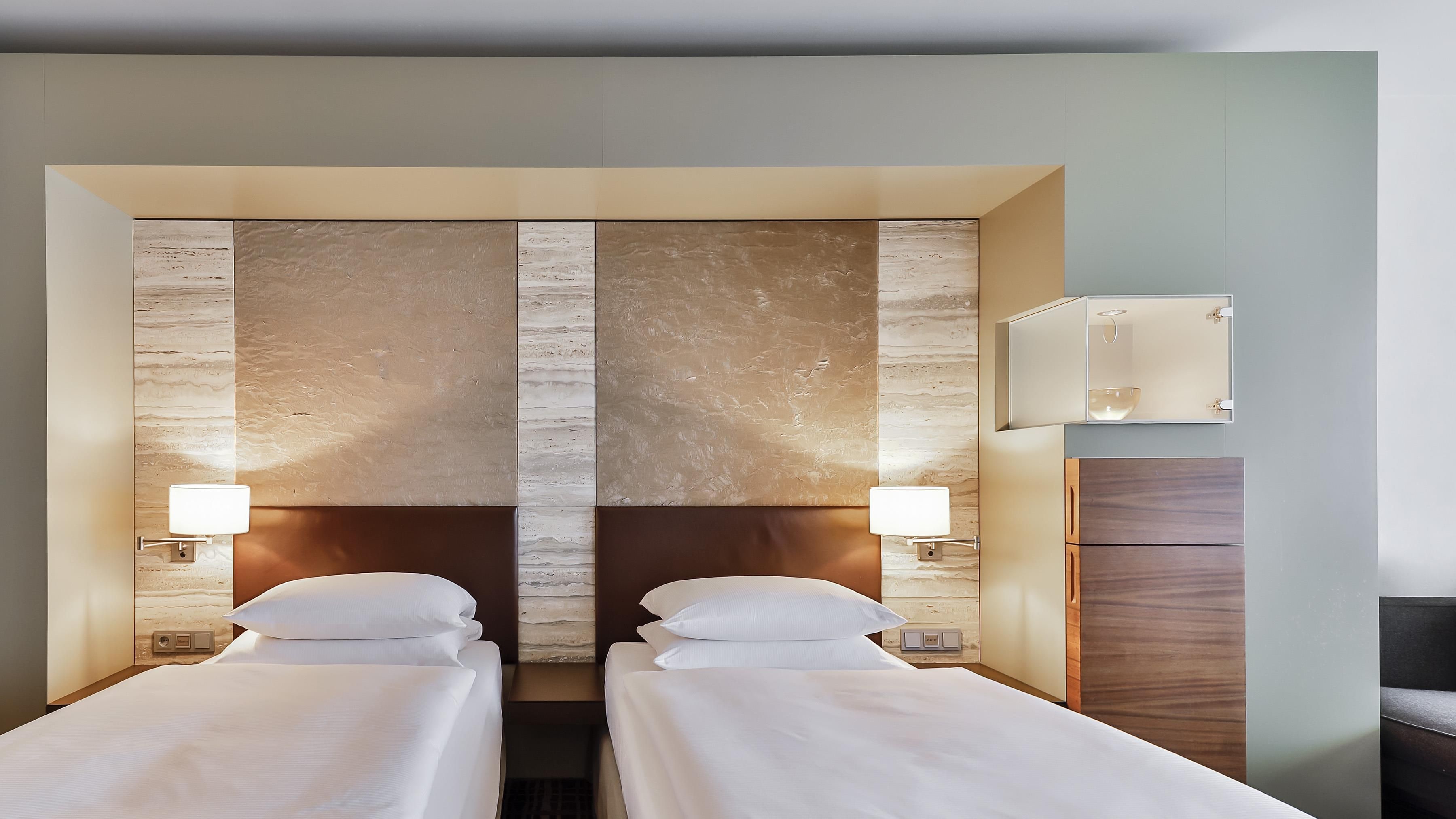 A hotel room with two beds, a wall-mounted light, and a bedside table.