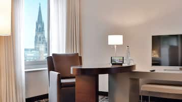 A hotel room with a large window, a chair, a table, a TV, and a lamp.