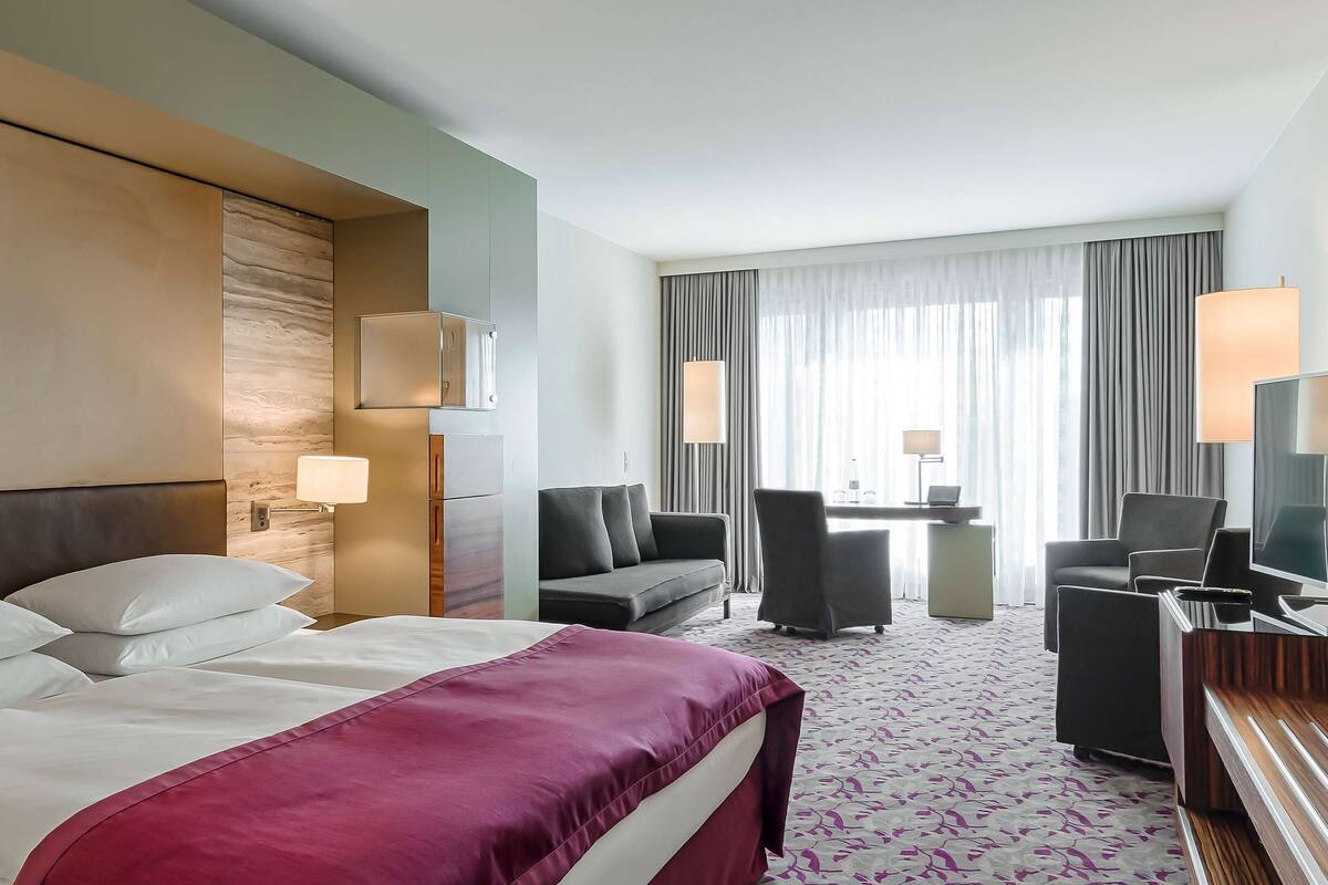 A hotel room with a bed, a desk, a TV, and a seating area.