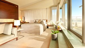 A hotel room with a large bed, a sofa, a nightstand, a potted plant, and a view of the city. - Dorint Hotel am Heumarkt Köln (Cologne)