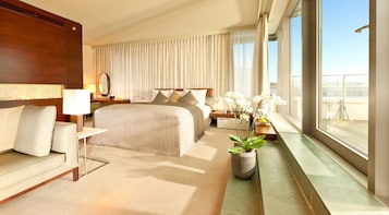 Habitación de hotel con una cama grande, un sofá, una mesita de noche, una planta en maceta y vistas a la ciudad.