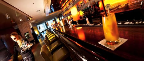 A bar area with a long counter, bar stools, and a well-stocked shelf with bottles and glasses.