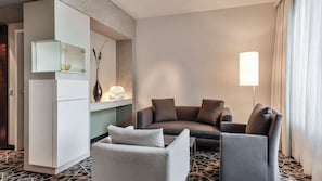 A modern hotel room with a sofa, armchair, and a minibar.