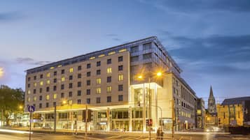 A modern hotel with a glass facade, multiple floors, and a prominent entrance.