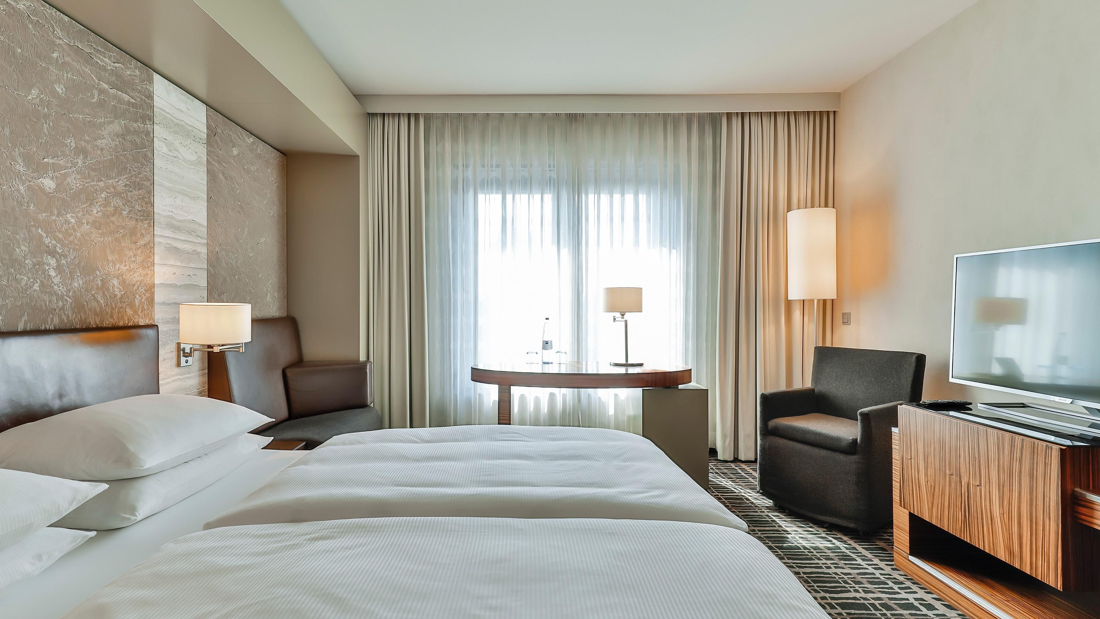 A hotel room with a large bed, a desk, a chair, and a television.