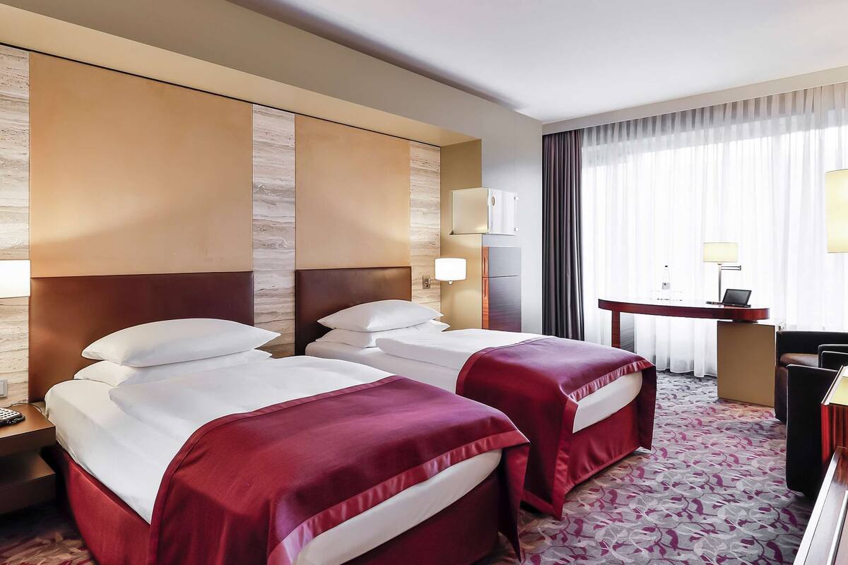 A hotel room with two beds, a desk with a chair, a TV, and a minibar.