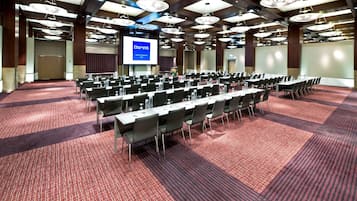 Ein Konferenzraum mit Tischen und Stühlen in Reihen, einem großen Bildschirm, der 'Dorint Hotel & Restaurant' zeigt, und einem roten Teppichboden.