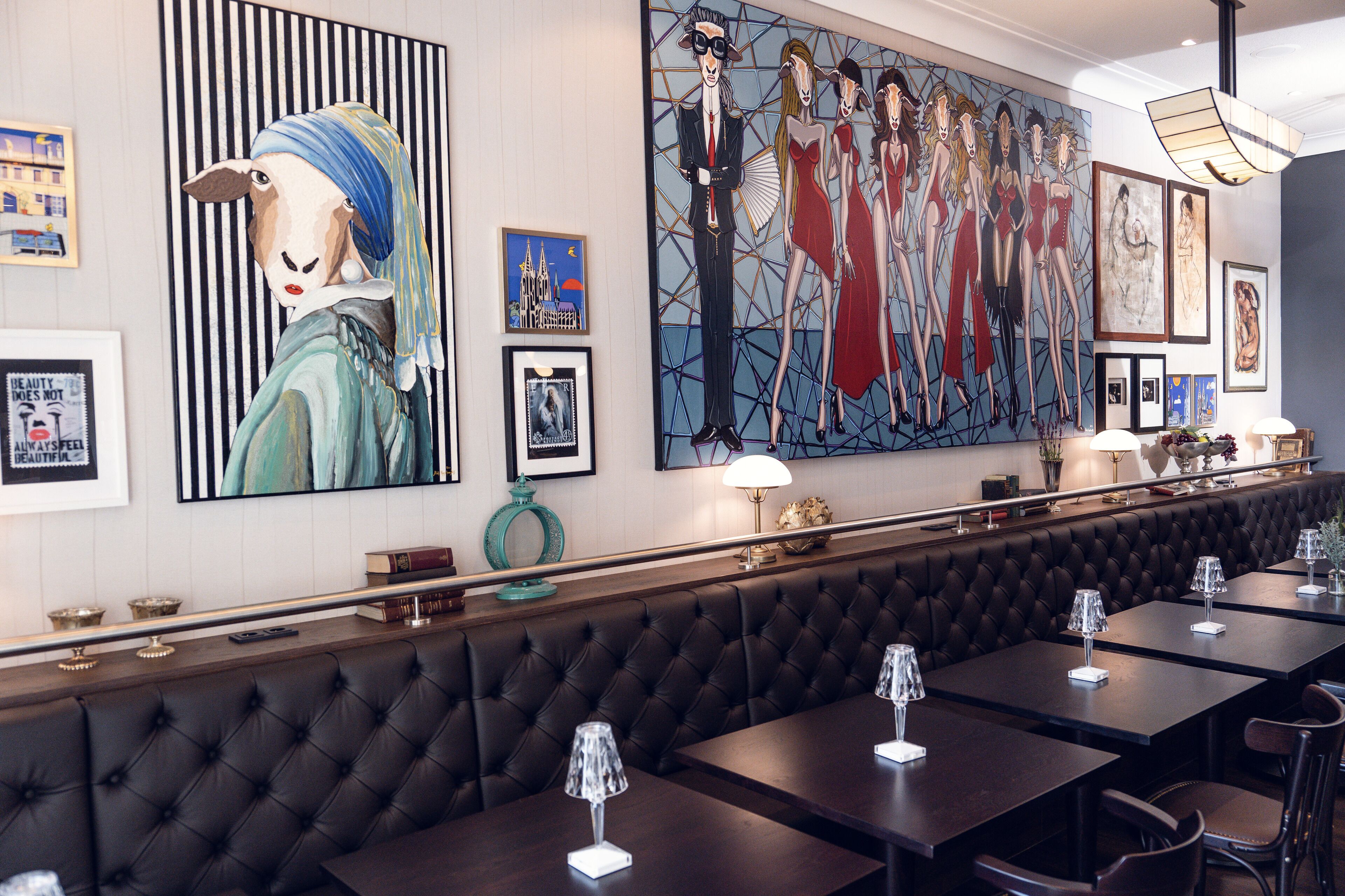 Un restaurante con una barra larga, asientos de cuero negro tipo cabina y un gran mural en la pared.