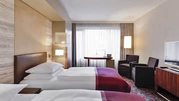 A hotel room with two beds, a desk with a lamp, a TV, and a chair.