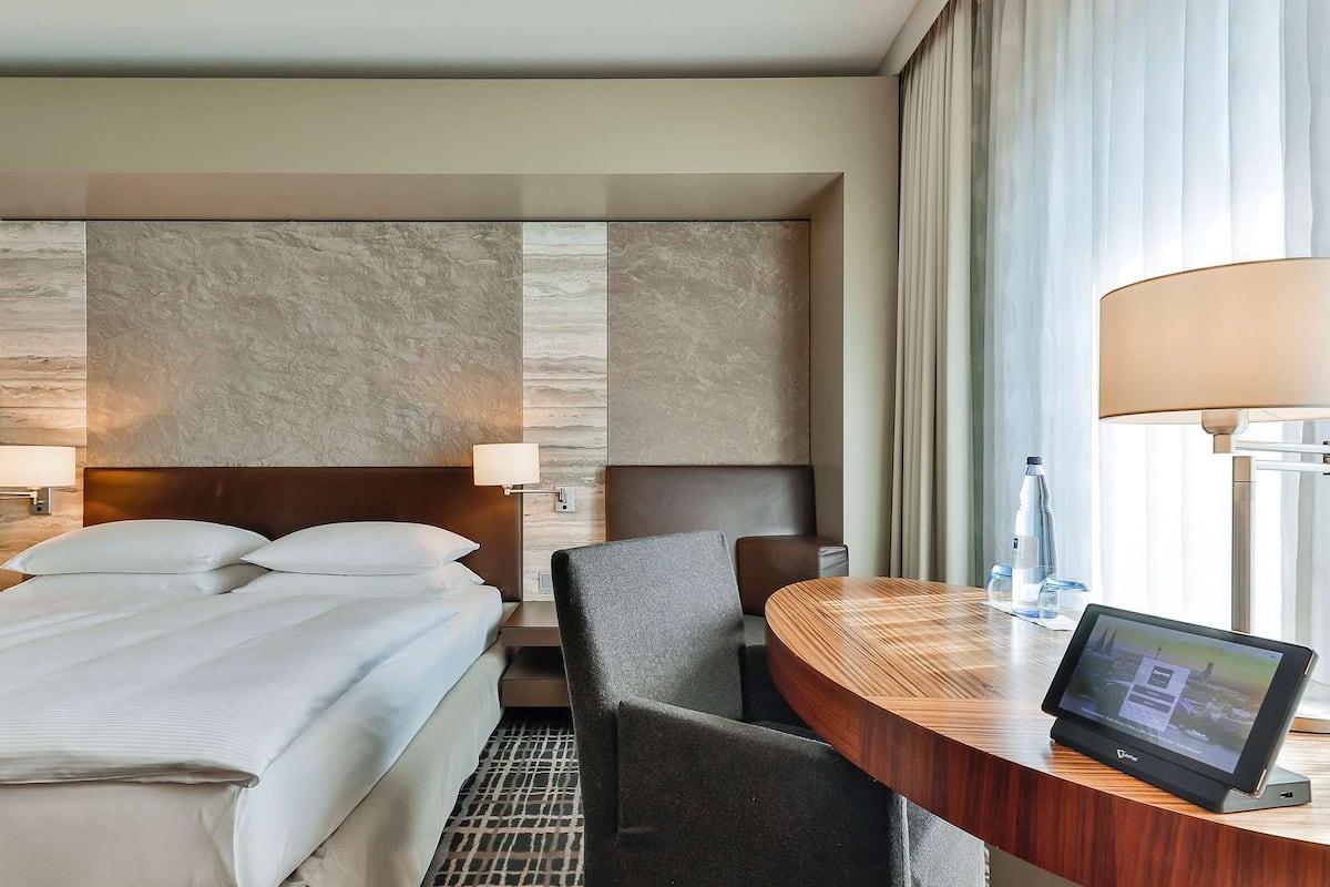 A hotel room with a bed, a desk with a computer, a chair, and a lamp.