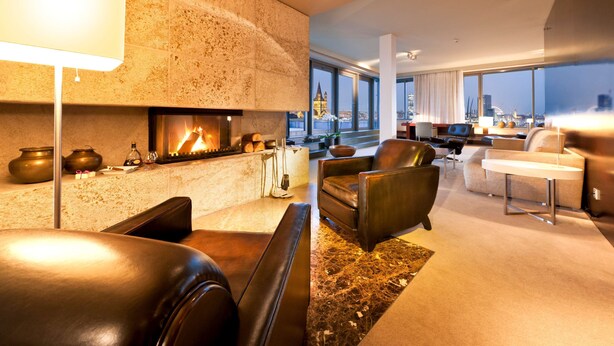 A modern living room with a fireplace, leather sofas, and a view of the cityscape through large windows. - Dorint Hotel am Heumarkt Köln (Cologne)