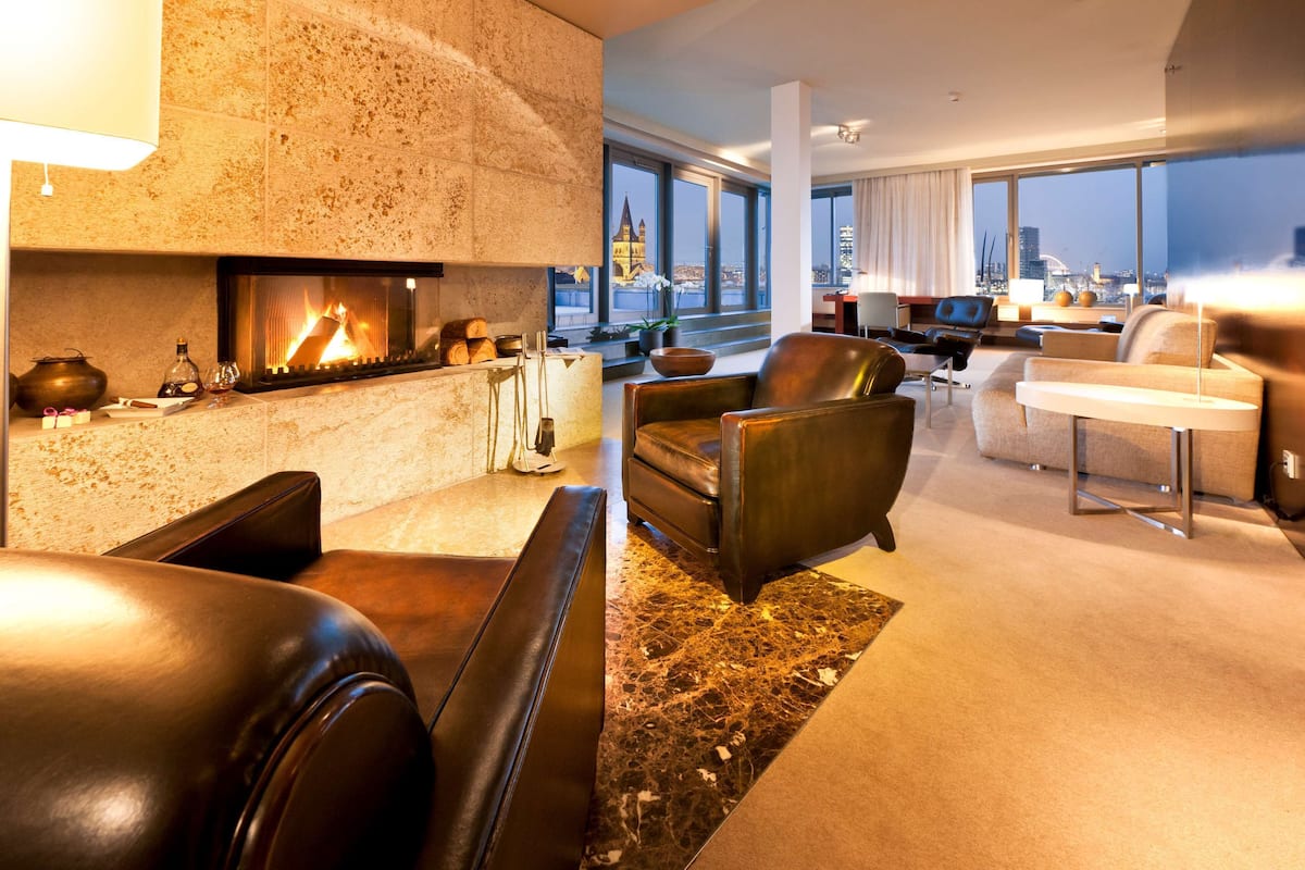 A modern living room with a fireplace, leather sofas, and a view of the cityscape through large windows.
