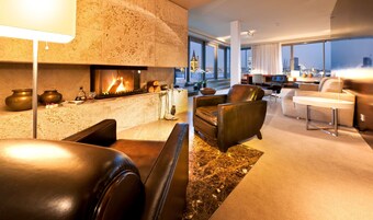 Una sala de estar moderna con chimenea, sofás de cuero y vistas de la ciudad a través de amplios ventanales.