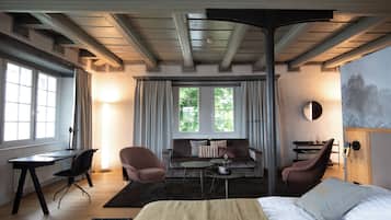 Ein Hotelzimmer mit einem Bett, einem Schreibtisch, zwei Stühlen, einem Sofa und einem großen Fenster mit Vorhängen.