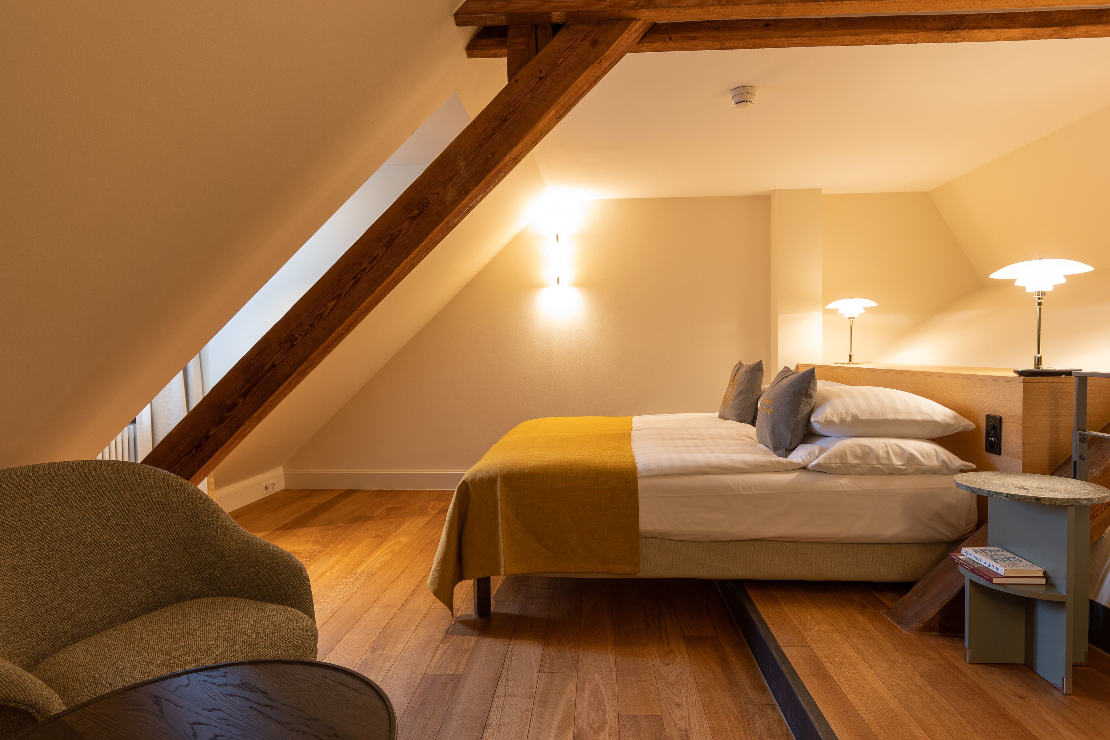 Un dormitorio con una cama, lámparas de noche, una silla y una mesita.