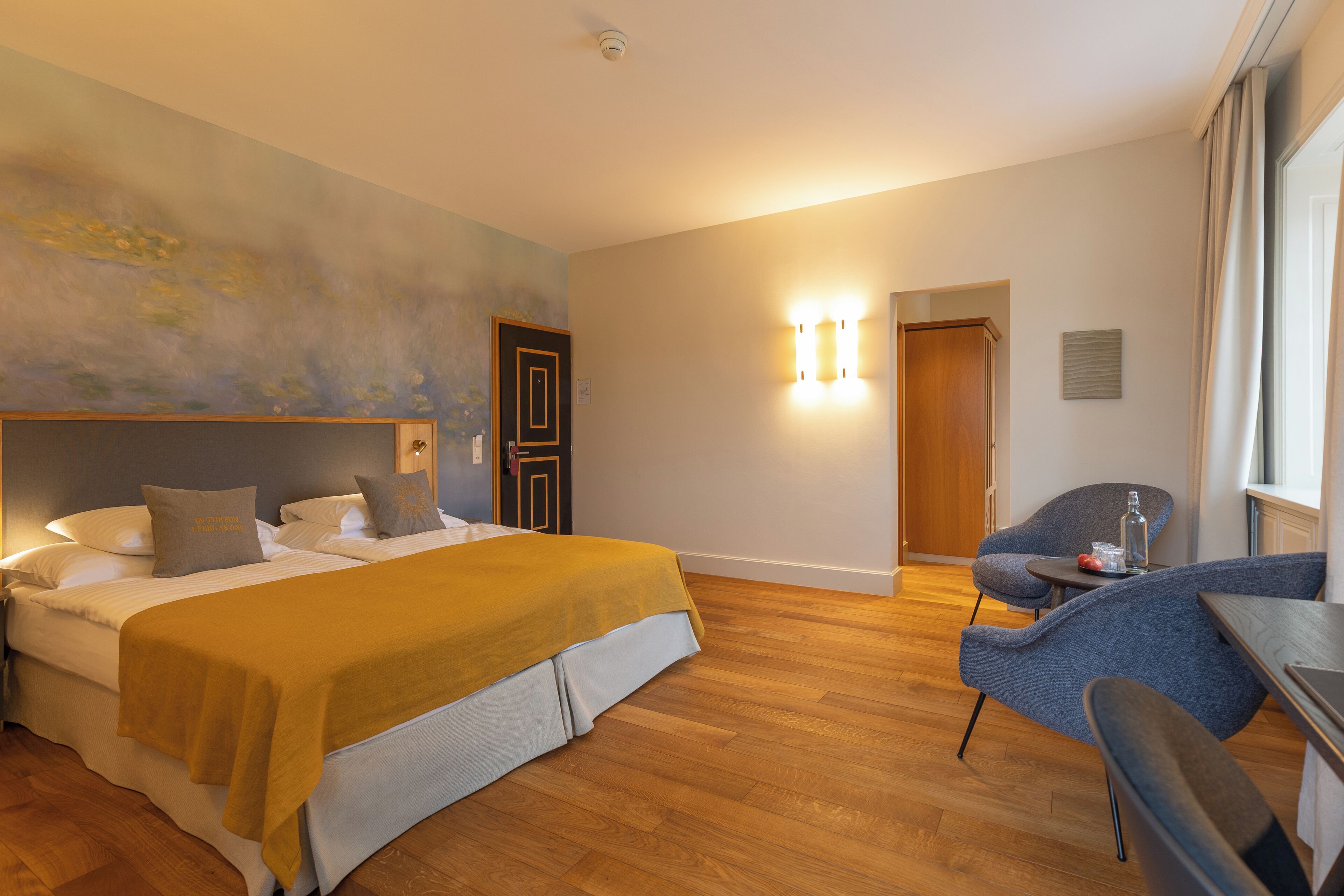 Ein Hotelzimmer mit Bett, Sessel, Tisch und Fenster.