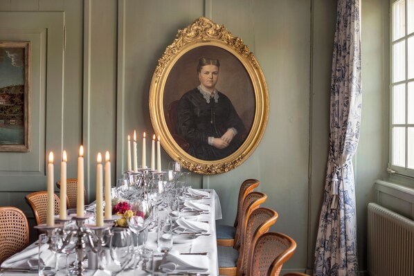 A dining room with a long table set for a meal, candles, and a framed portrait on the wall. - Boutiquehotel Sonne (Kuesnacht)