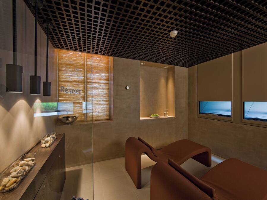 A modern spa room with a wooden reception desk, two cushioned seating areas, and a ceiling with a grid pattern.