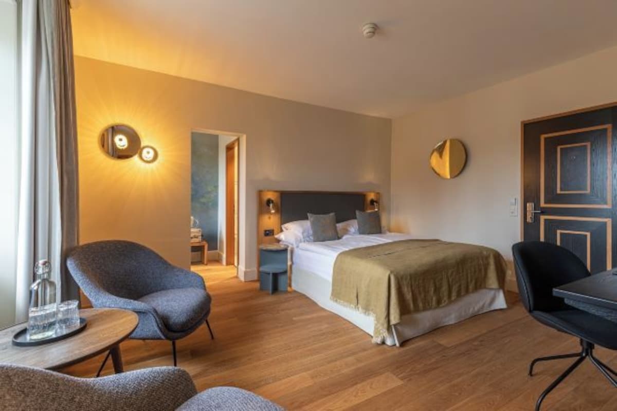 Habitación de hotel con cama, escritorio, silla, mesa redonda y lámpara de pared.