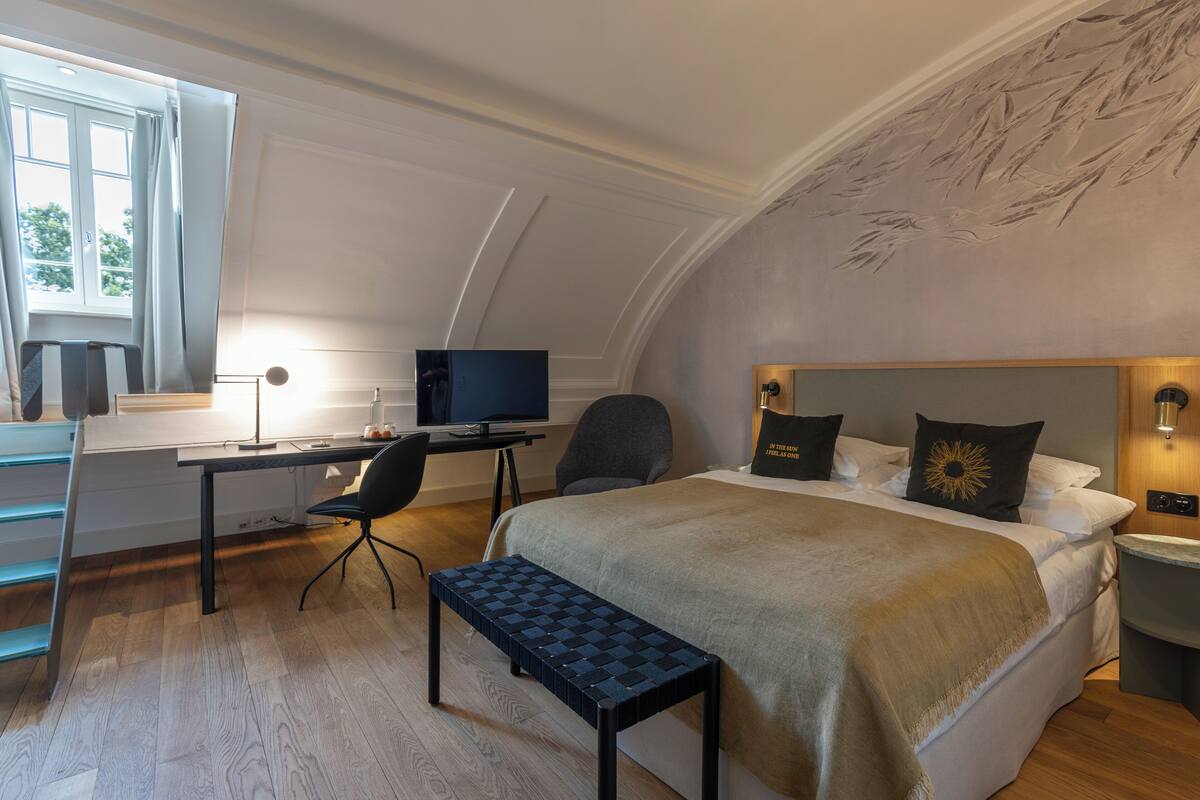 A modern bedroom with a bed, desk, chair, and a small bench.