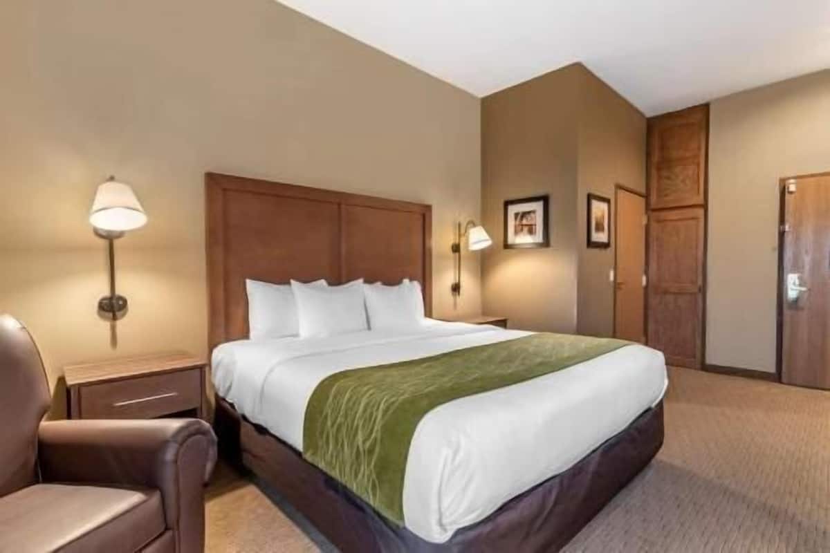 Une chambre d’hôtel avec un lit, une table de chevet, une lampe, une chaise et une porte.