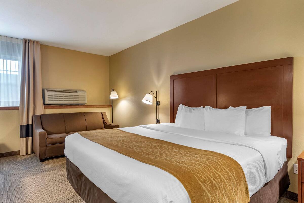 Une chambre d’hôtel avec un grand lit, un canapé, un appareil de climatisation et deux lampes fixées au mur.
