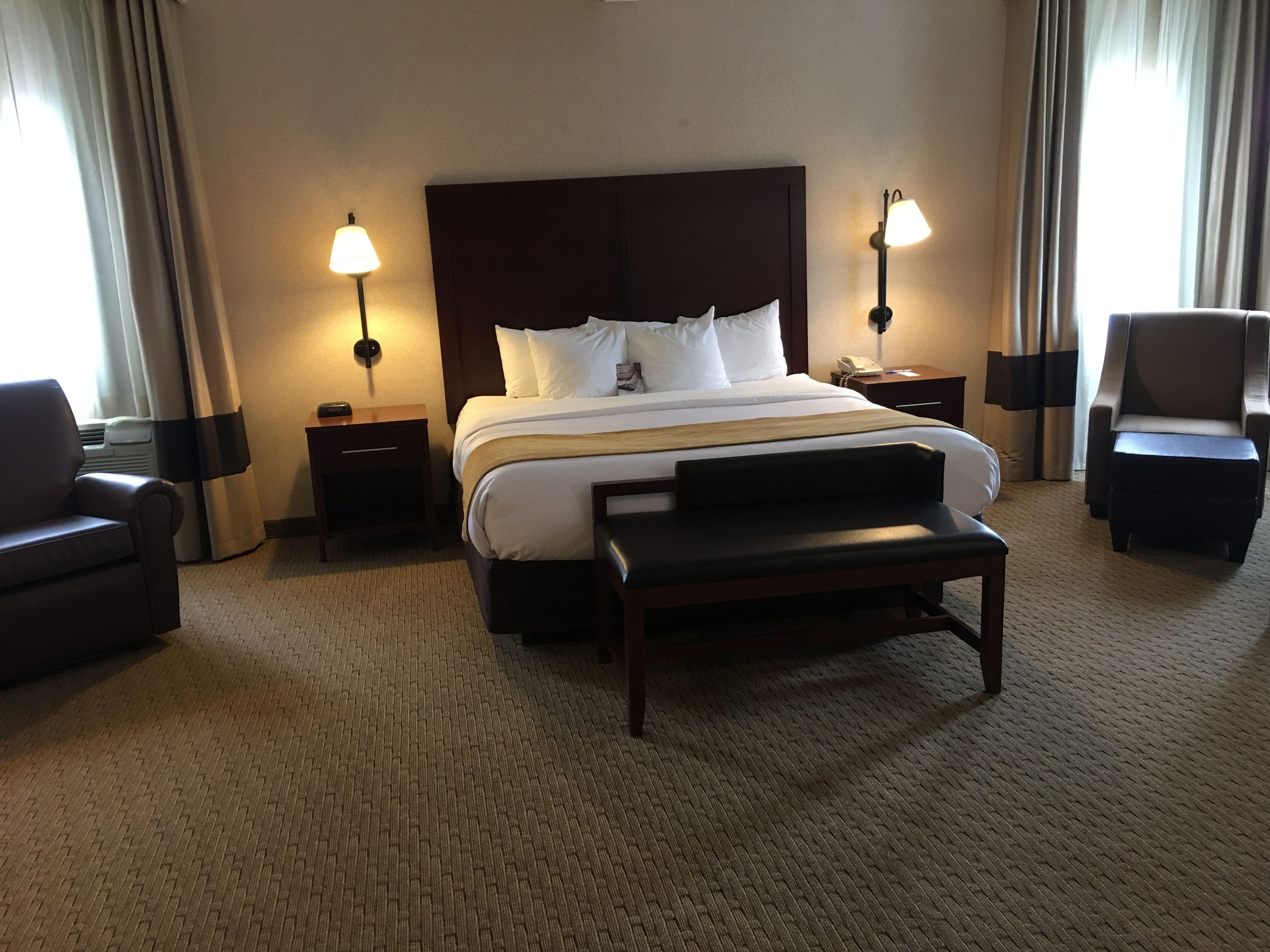 A hotel room with a large bed, two bedside tables with lamps, a chair, and a desk.