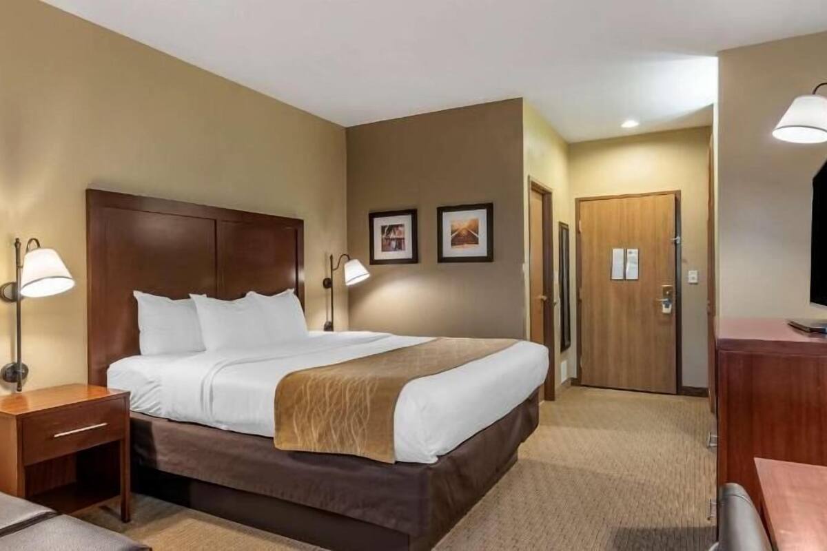 A hotel room with a bed, bedside tables, a desk, a chair, a TV, and a door.