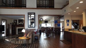 A spacious hotel lobby with a high ceiling, wooden flooring, a seating area with a table and chairs, a kitchen area, and a staircase leading to an upper level. - Comfort Inn Warrensburg Station (Warrensburg)