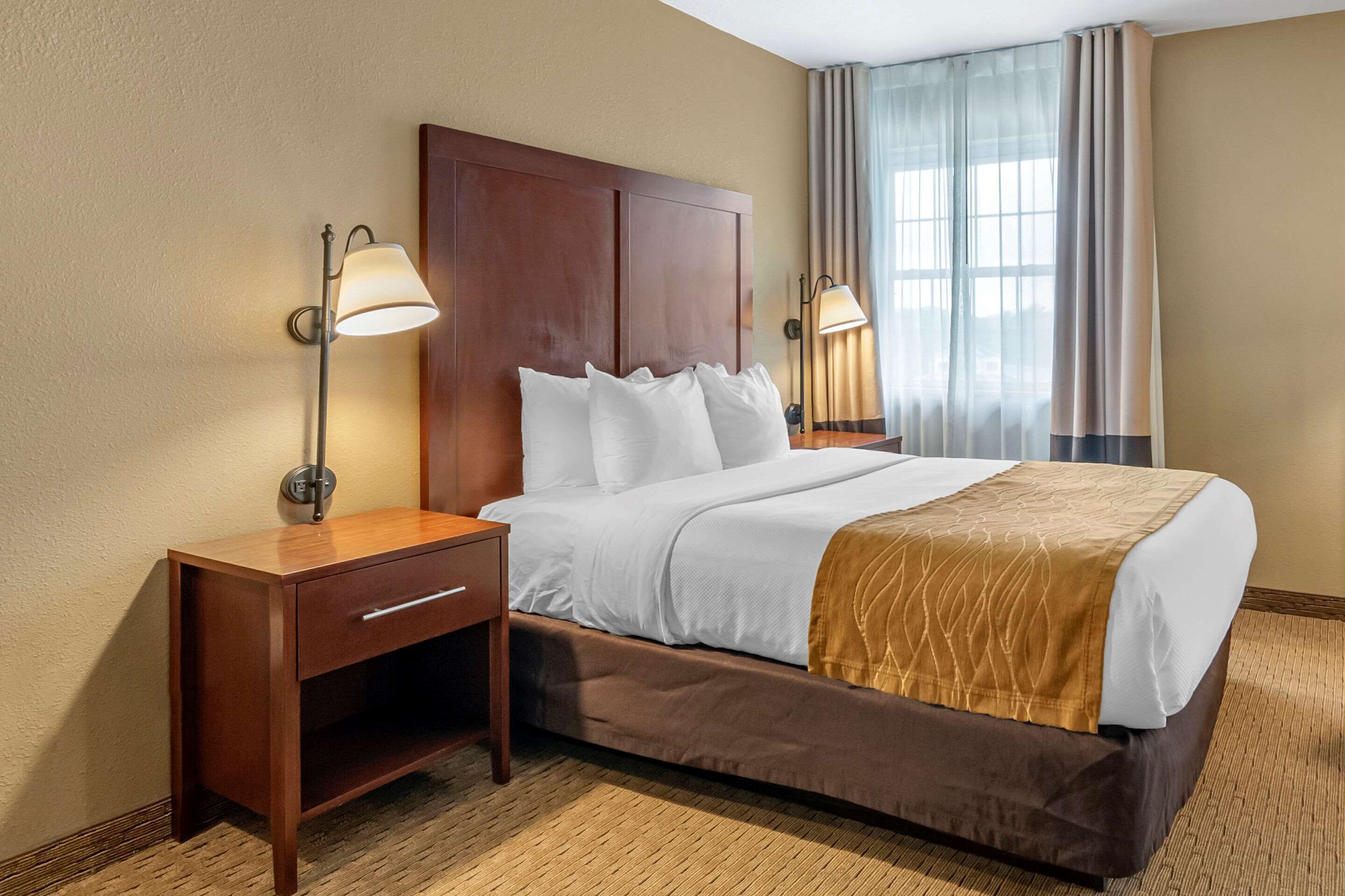 A hotel room with a large bed, two bedside tables, a wooden nightstand, and a window with curtains.